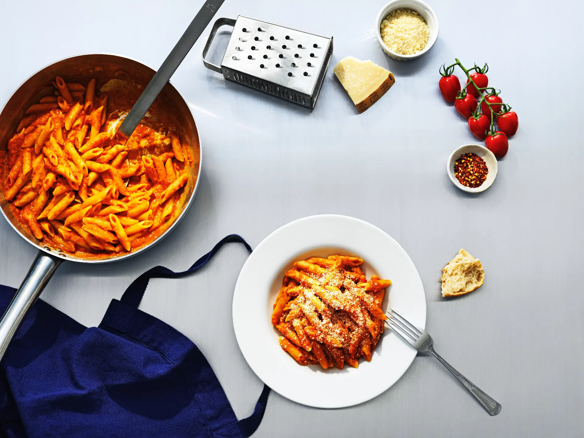 Penne i krämig pastasås i panna och upplagd på tallrik, med parmesan, körsbärstomater och chili